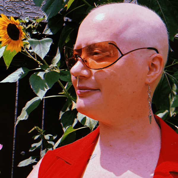 side profile of a woman in sunglasses, standing in front of some sunflowers.