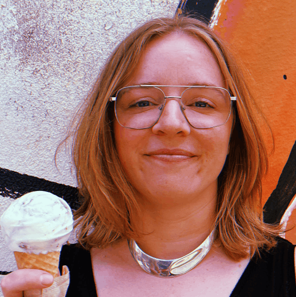 a woman smiling with glasses and a silver necklace, holding an ice cream cone.